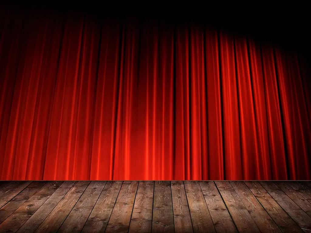 Ein roter, geschlossener Theatervorhang mit einer hölzernen Bühne im Vordergrund
