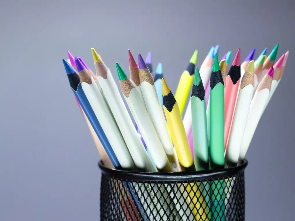 ein Behälter mit vielen Buntstiften in verschiedenen Farben vor grauem Hintergrund