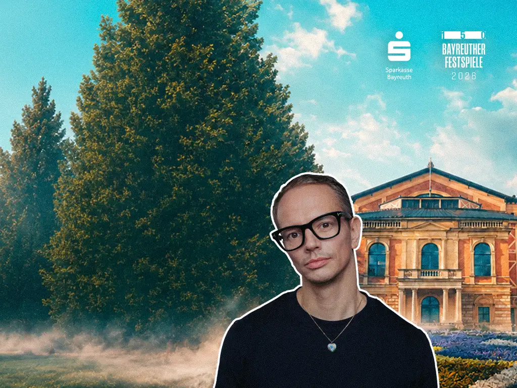 DJ Alle Farben, wearing glasses and a necklace, in front of a large tree and the historic Festspielhaus